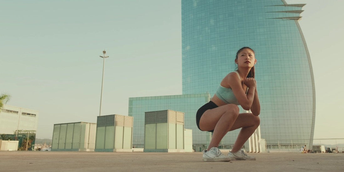 Young Asian woman performing squats in front of a high-rise building.